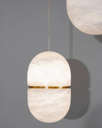 A Clérachic alabaster capsule with its gold band, lit softly against a grey wall, with part of a second shade at the top right.