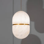 A Clérachic alabaster pendant with a gold band, glowing against a grey wall with soft shadows of other shades behind it.