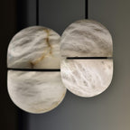 Close view of two Clérachic alabaster pendants with dark bands, the stone glowing with brown and white veins.