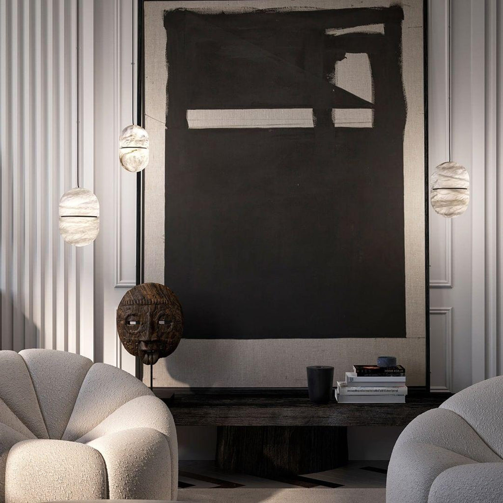 Three Clérachic alabaster pendants around a large dark artwork, above boucle armchairs and a console with books.