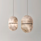 Two Clérachic alabaster pendants of different sizes on a pale grey backdrop, their dark bands and veined stone clear to see.