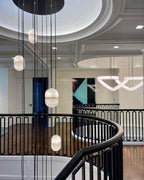 Clérachic alabaster pendants hanging on black cords through a stair hall with a black railing and a coffered ceiling.