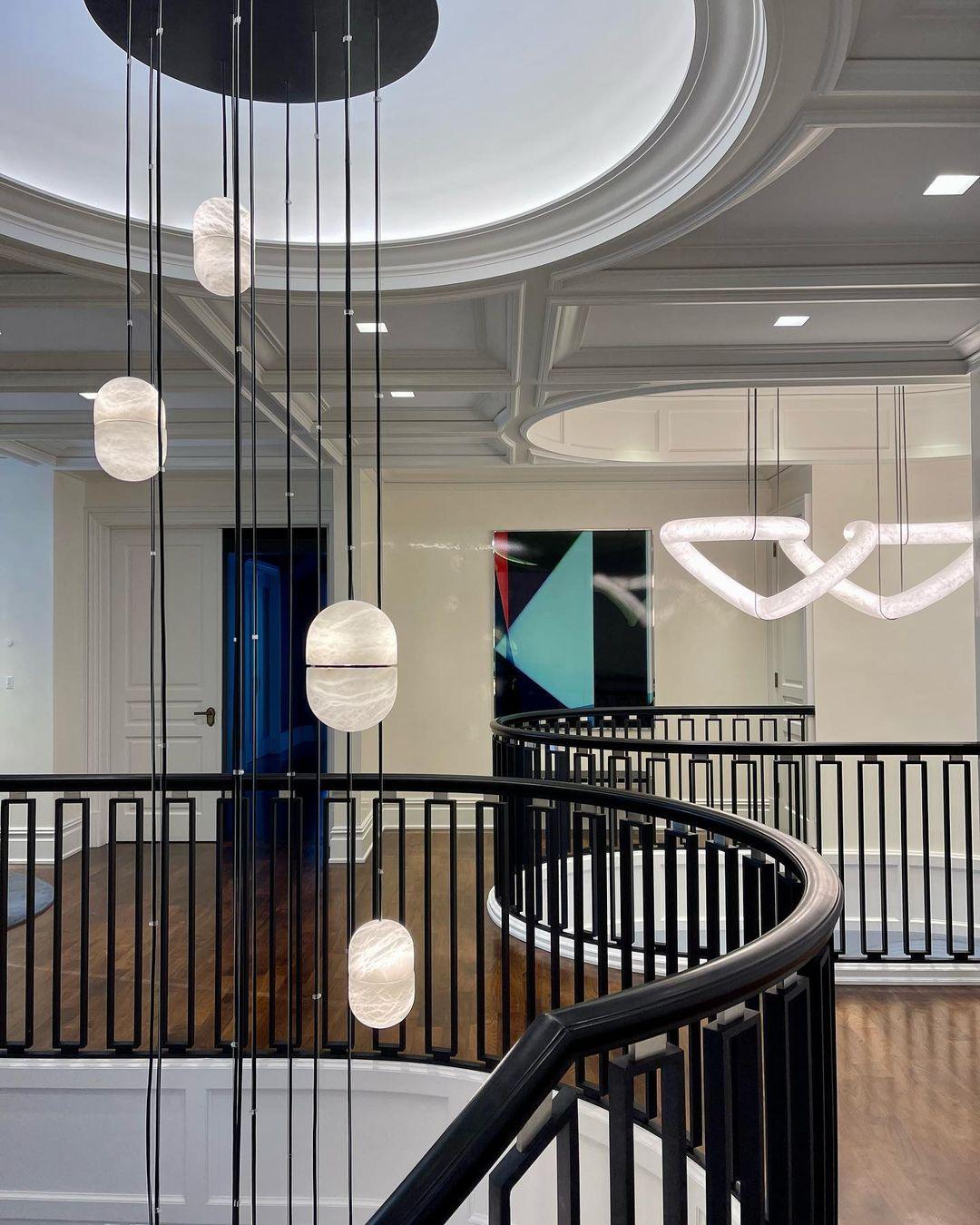 Clérachic alabaster pendants hanging on black cords through a stair hall with a black railing and a coffered ceiling.