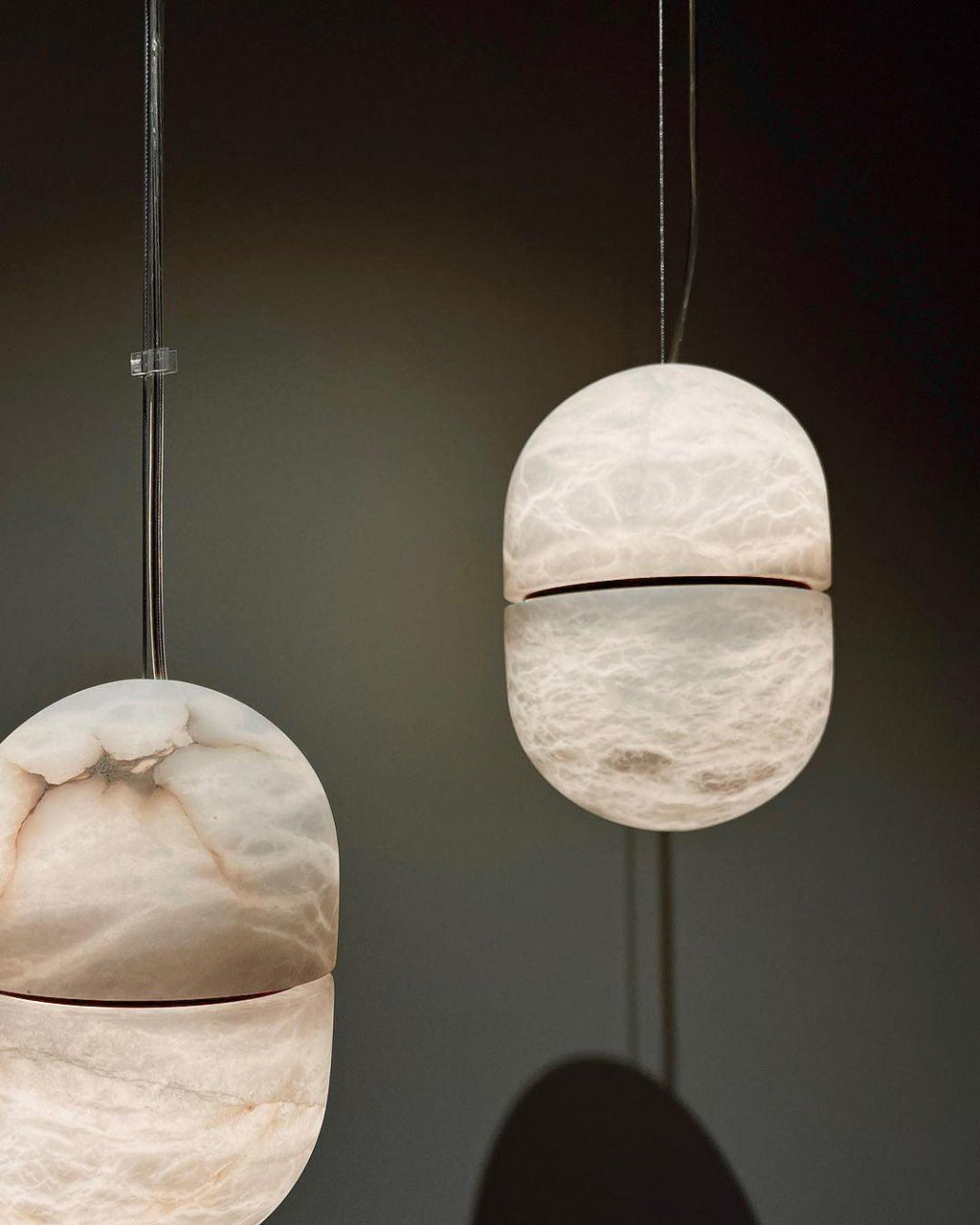 Two Clérachic alabaster pendants on a dark backdrop, with a larger shade at the lower left and a smaller one at the right.