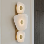 Clérachic alabaster wall sconce mounted on panelled cream wall beside a dark oak door, warm light ringing each brass disc.