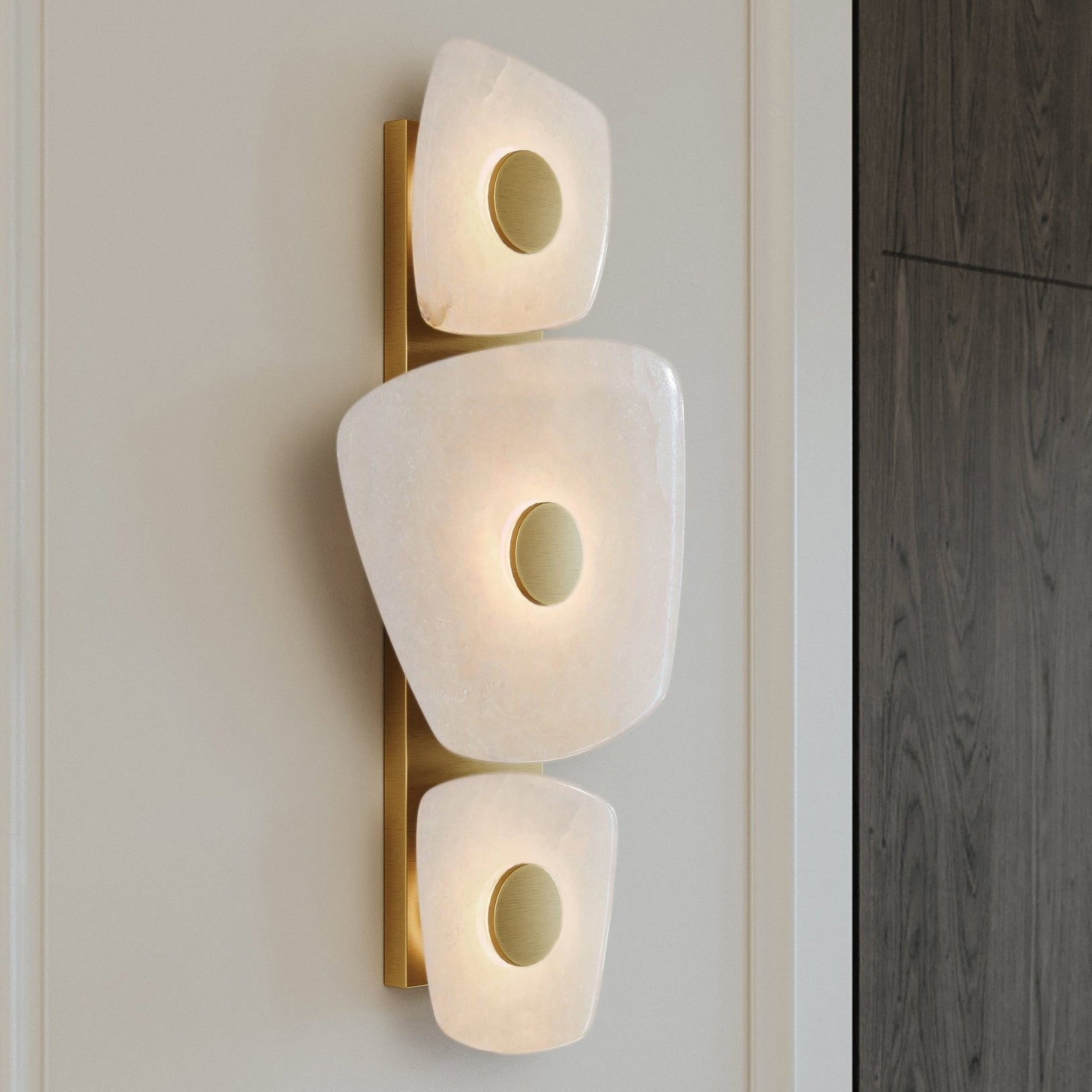 Clérachic alabaster wall sconce mounted on panelled cream wall beside a dark oak door, warm light ringing each brass disc.