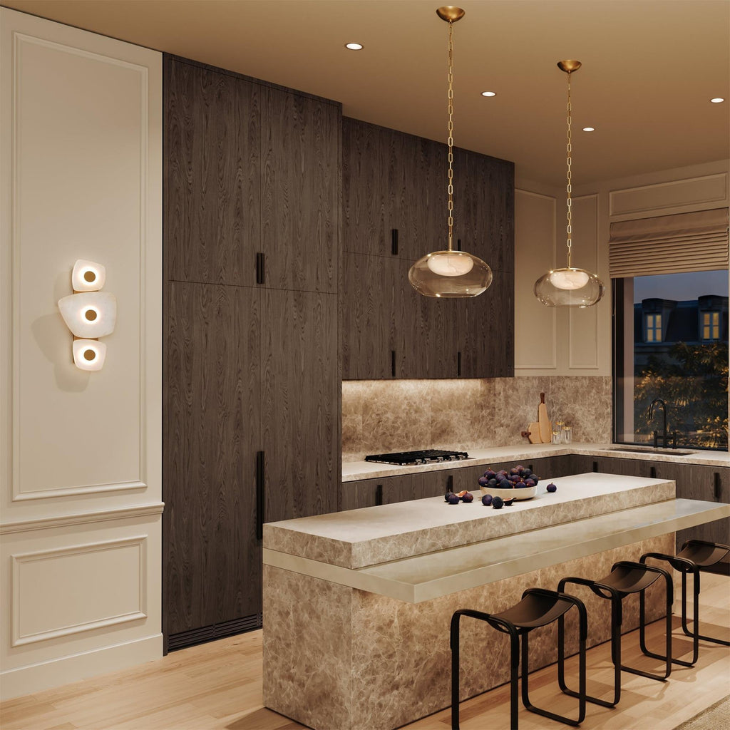 Clérachic alabaster wall sconce lit after dark in a kitchen, its glow warm against the cream panelling beside it.