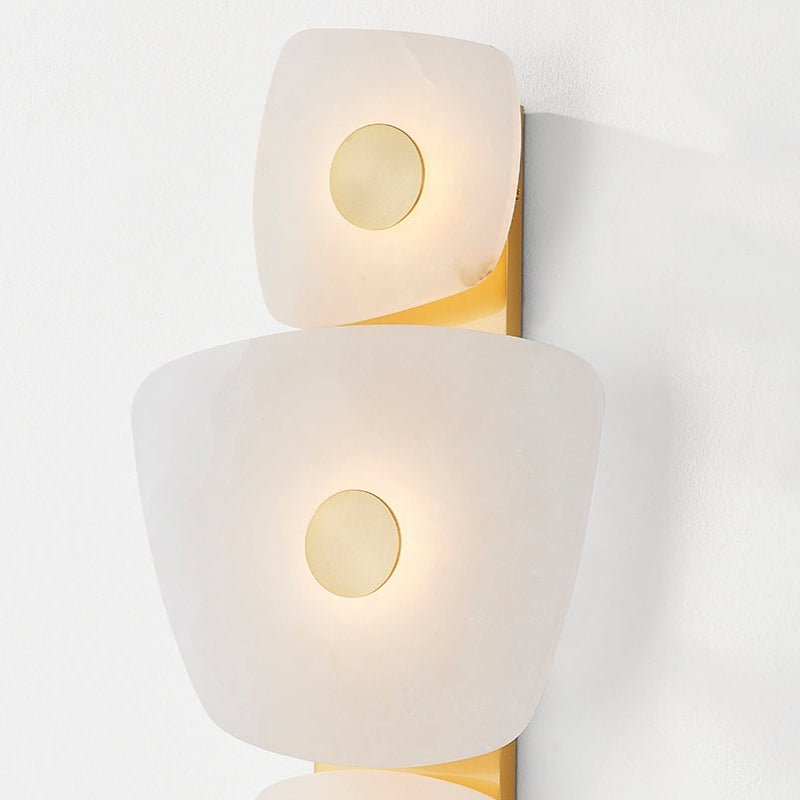 Close crop of the Clérachic alabaster wall sconce, light haloing the brass disc at the centre of each alabaster plate.