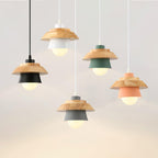 Five Clérachic pendants in black, white, green, grey and pink hang at different heights, each with a wood top and a bulb glowing inside.