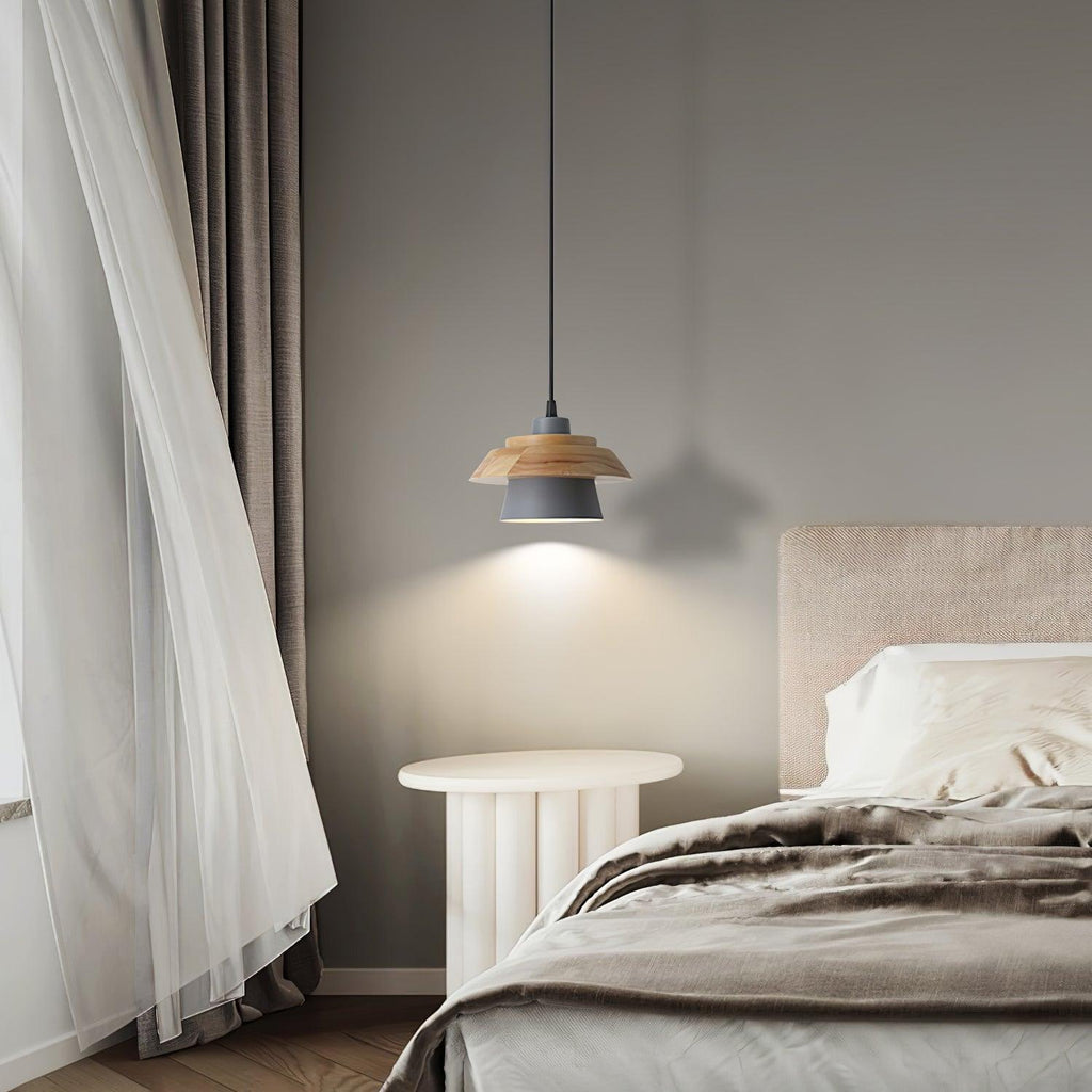 A small grey-shaded Clérachic pendant hangs beside a bed with a sheer curtain and a pale fluted round side table.