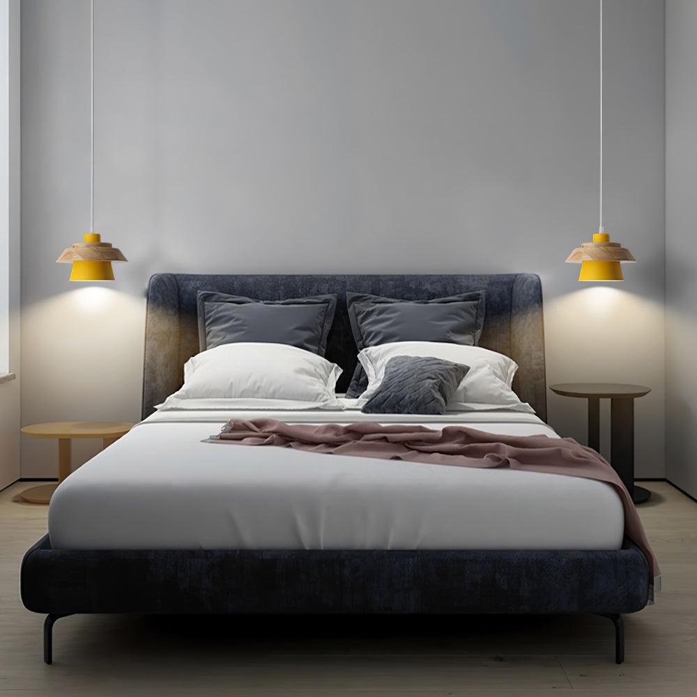 Two yellow-shaded Clérachic pendants hang either side of a dark upholstered bed in a grey bedroom.