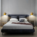 Two yellow-shaded Clérachic pendants hang either side of a dark upholstered bed in a grey bedroom.