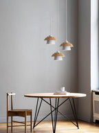 Three white-shaded Clérachic pendants hang at different heights above a round wooden table with a metal base and a wooden chair.