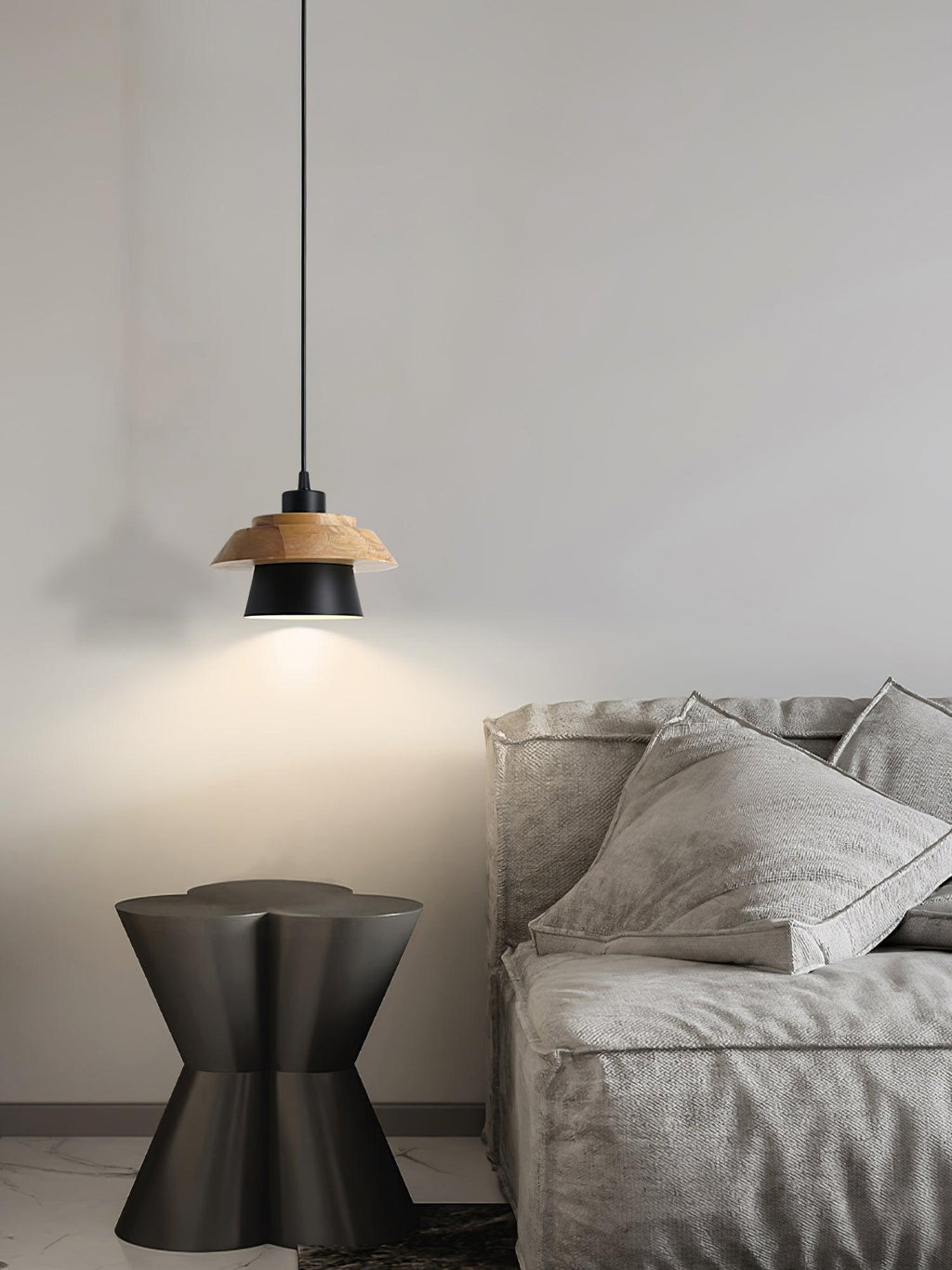 A black-shaded Clérachic pendant with a wood top hangs over a grey sofa and a dark sculptural side table.