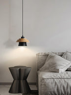 A black-shaded Clérachic pendant with a wood top hangs over a grey sofa and a dark sculptural side table.