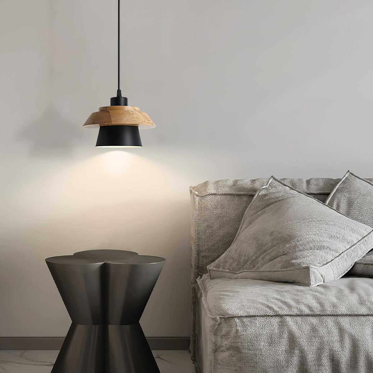 A black-shaded Clérachic pendant with a wood top lights a nubbly grey sofa, beside a dark hourglass-shaped side table.