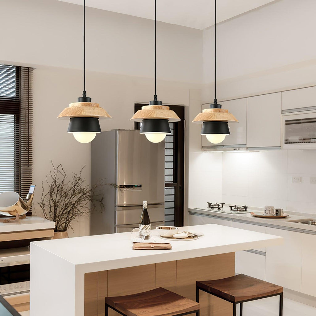 Three black-shaded Clérachic pendants with bulbs glowing hang over a white kitchen island with wooden stools.