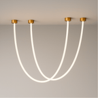 Clérachic gold-capped flexible LED chandelier arcs in three glowing loops of different lengths on a grey wall.