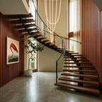 Clérachic gold-capped flexible LED chandelier cascades in multiple loops above a curved staircase and framed art.