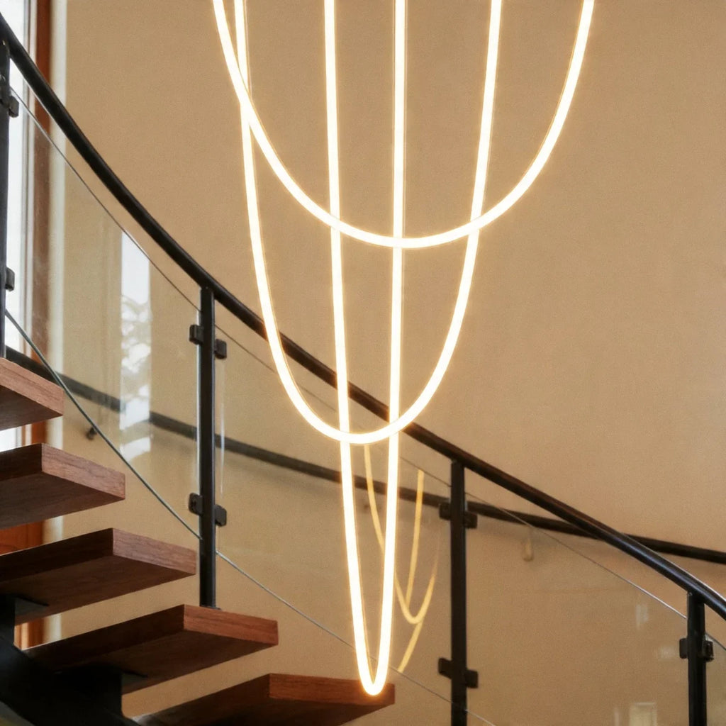 Close view of the Clérachic flexible LED chandelier's glowing loops crossing beside a black stair railing.