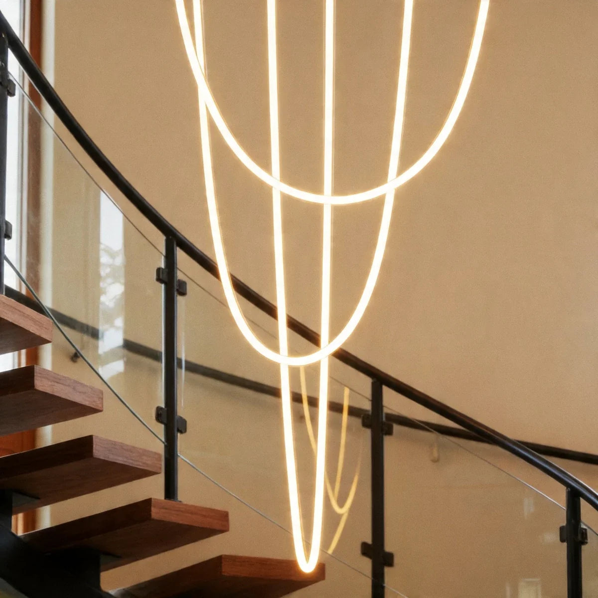 Close view of the Clérachic flexible LED chandelier's glowing loops crossing beside a black stair railing.