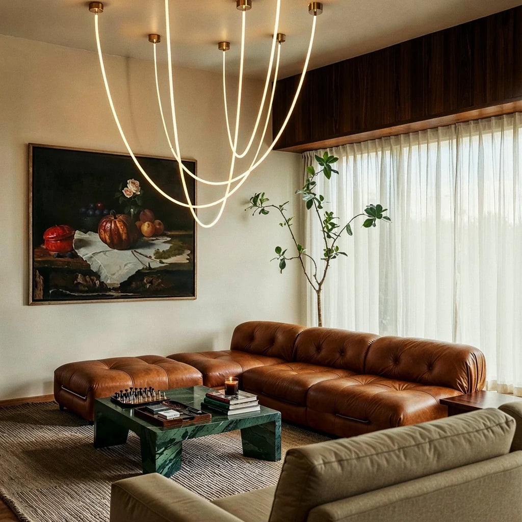 Clérachic gold-capped flexible LED chandelier arcs in six loops above a tan leather sofa and framed still life.