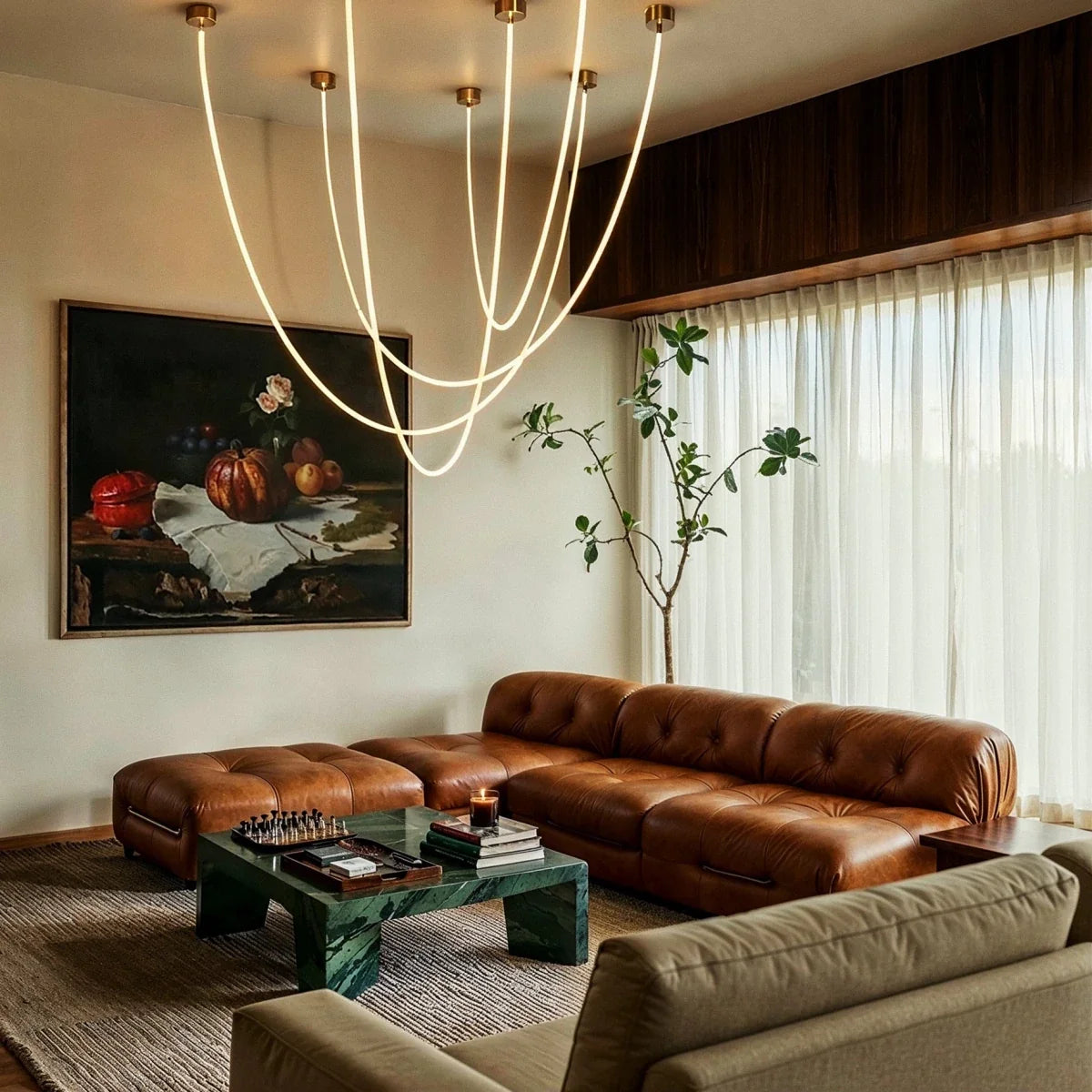 Clérachic gold-capped flexible LED chandelier arcs in six loops above a tan leather sofa and framed still life.