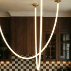 Close view of the Clérachic flexible LED chandelier's glowing loops against checkerboard tile and walnut cabinets.