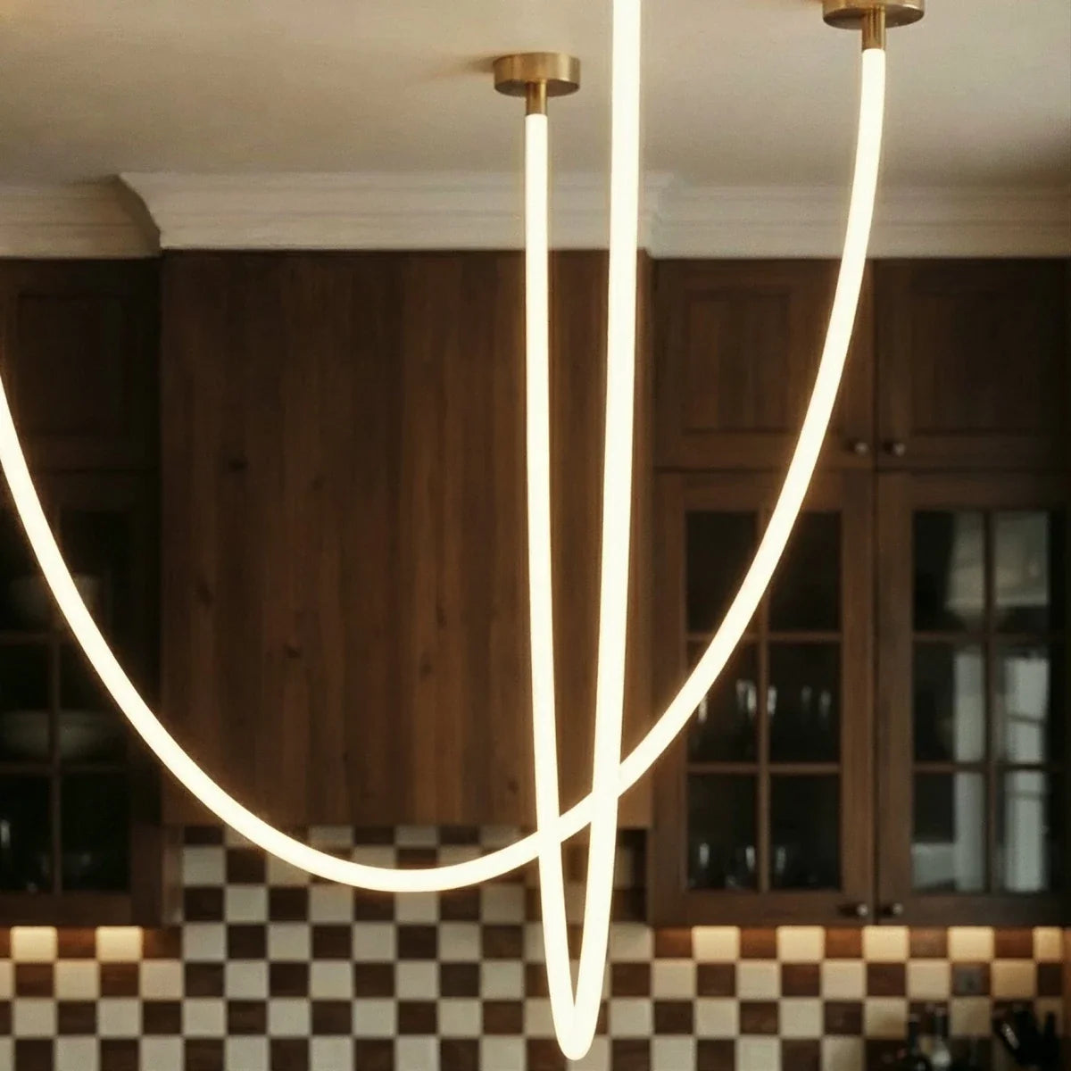 Close view of the Clérachic flexible LED chandelier's glowing loops against checkerboard tile and walnut cabinets.