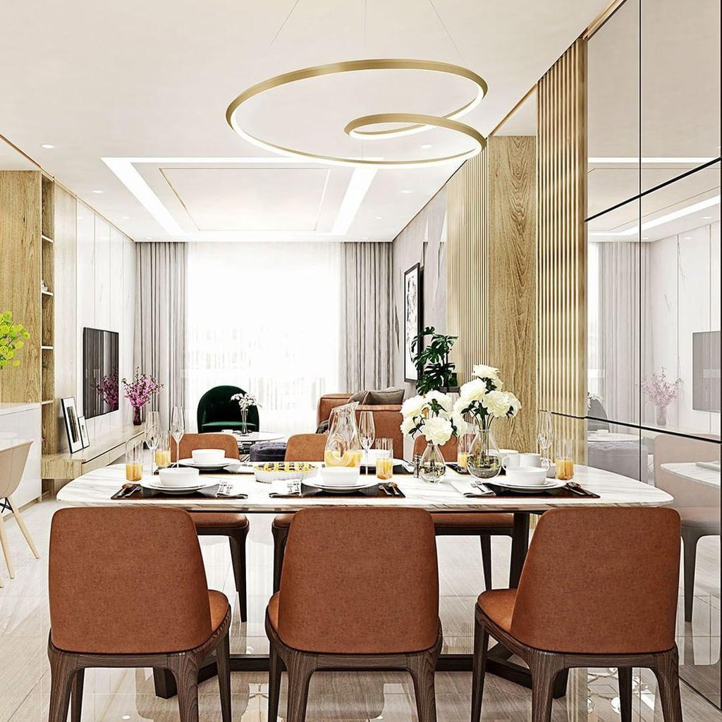 This Clérachic gold ring chandelier curls above a long dining table with rust-brown chairs, in a bright room with timber slats.