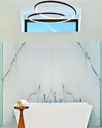 Clérachic ring chandelier in black, lit, above a freestanding white bath and a marble wall, seen through a ceiling recess.