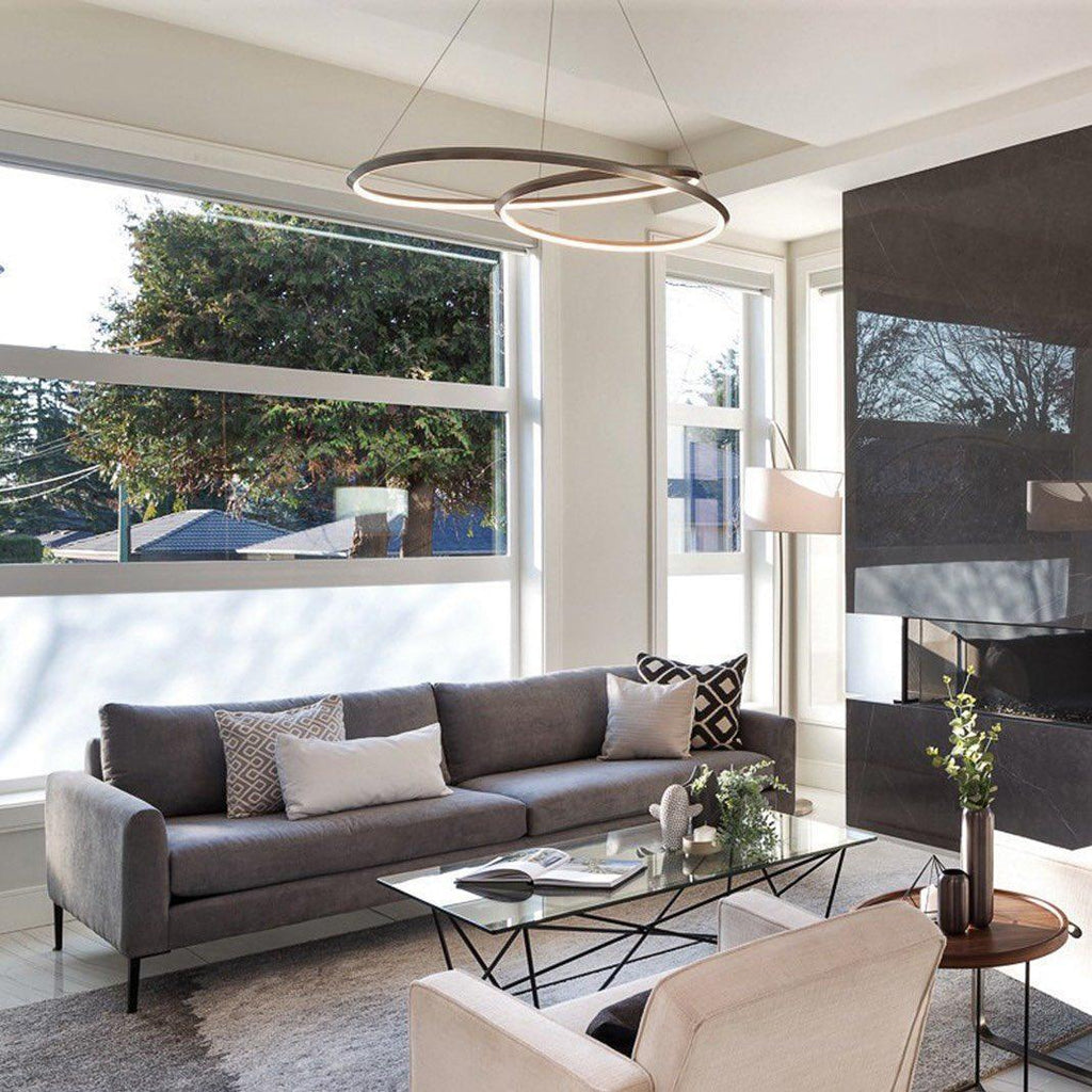 A bronze-toned ring chandelier from Clérachic in a bright living room, above a grey sofa and a glass coffee table.