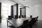 Black nested ring chandelier from Clérachic over a long dark meeting table with black chairs, in a room with white brick walls.