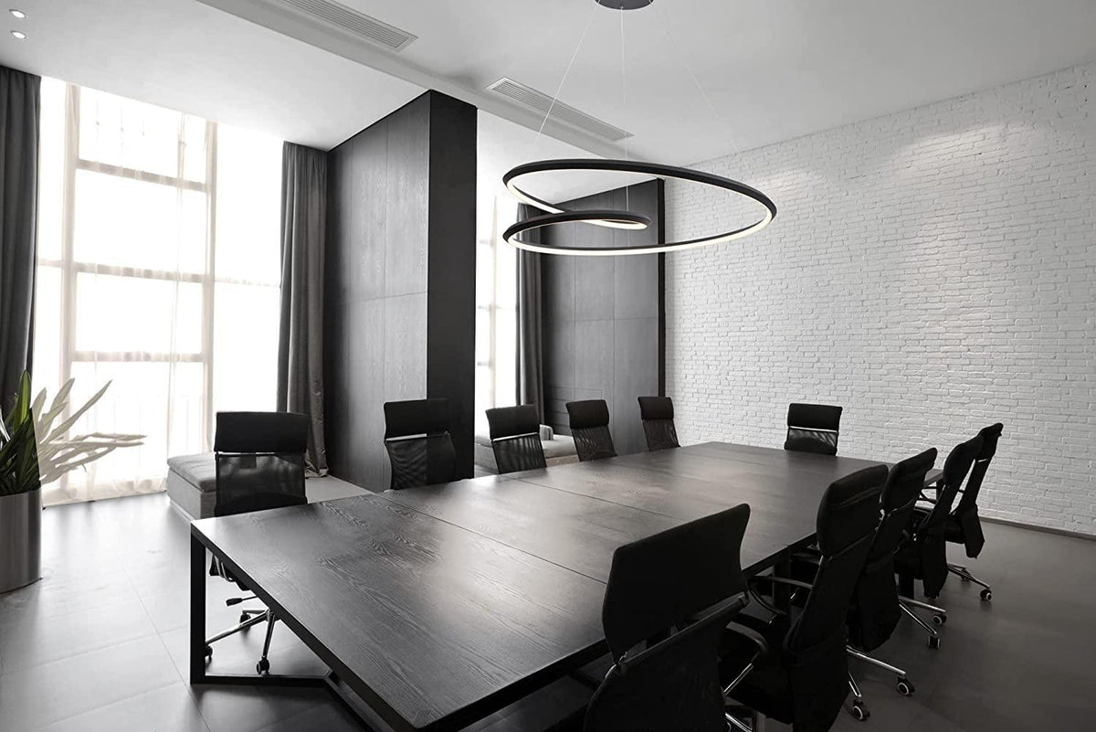 Black nested ring chandelier from Clérachic over a long dark meeting table with black chairs, in a room with white brick walls.