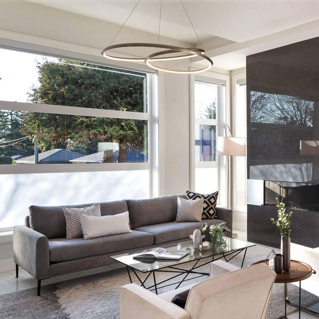 Brown-bronze ring chandelier from Clérachic above a grey sofa, with large windows and a glass coffee table below.