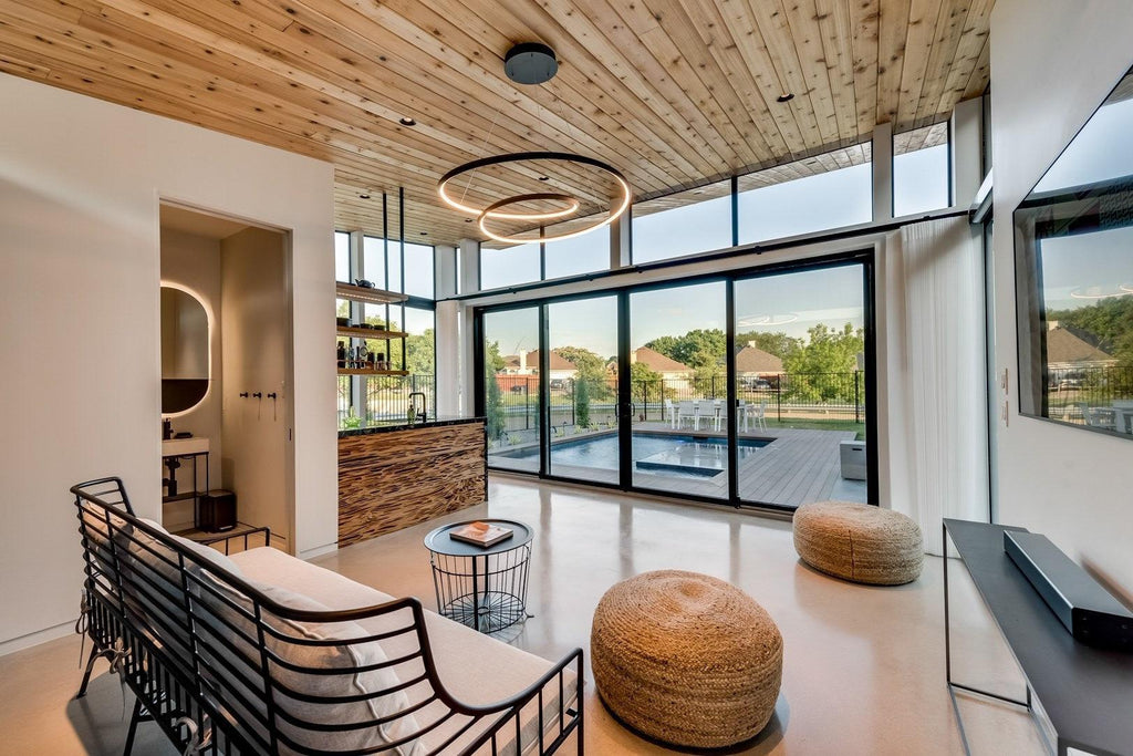 Black ring chandelier from Clérachic hung from a timber ceiling in an open living area with a black metal sofa and a pouffe.
