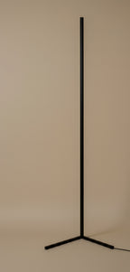 The floor lamp switched off in daylight, showing the matte black square-section bar and the three flat blades of its base