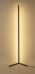 Clérachic Nordic LED floor lamp lit, its slim black bar throwing a soft warm wash onto the wall behind it from a low three-blade base
