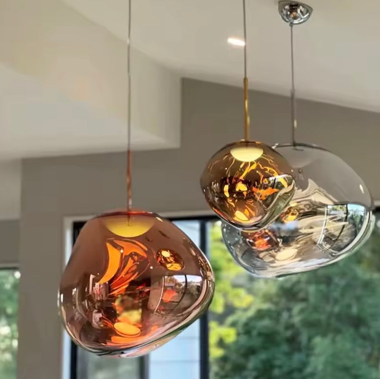 Three Clérachic melt pendants lit above a kitchen counter in copper, amber and chrome.