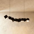 Clérachic row of eight tilted black aluminium cubes on two cables, each cube glowing white from below, against plaster.
