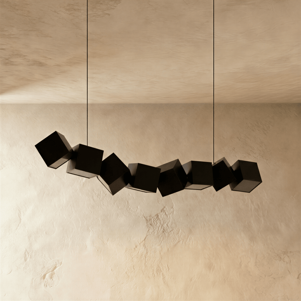 Clérachic row of eight tilted black aluminium cubes hung on two cables, switched off, against a limewashed wall.