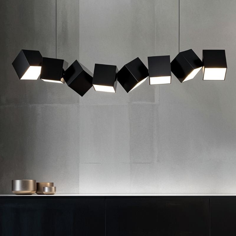 Clérachic eight black aluminium cubes hung at offset angles over a dark sideboard, each lit from below, on a grey wall.