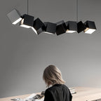 Clérachic eight black aluminium cubes in a tilted row above a pale wooden table where a person sits reading.