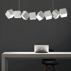 Clérachic eight white aluminium cubes in a tilted row above a white desk with a laptop and black chair on a charcoal wall.