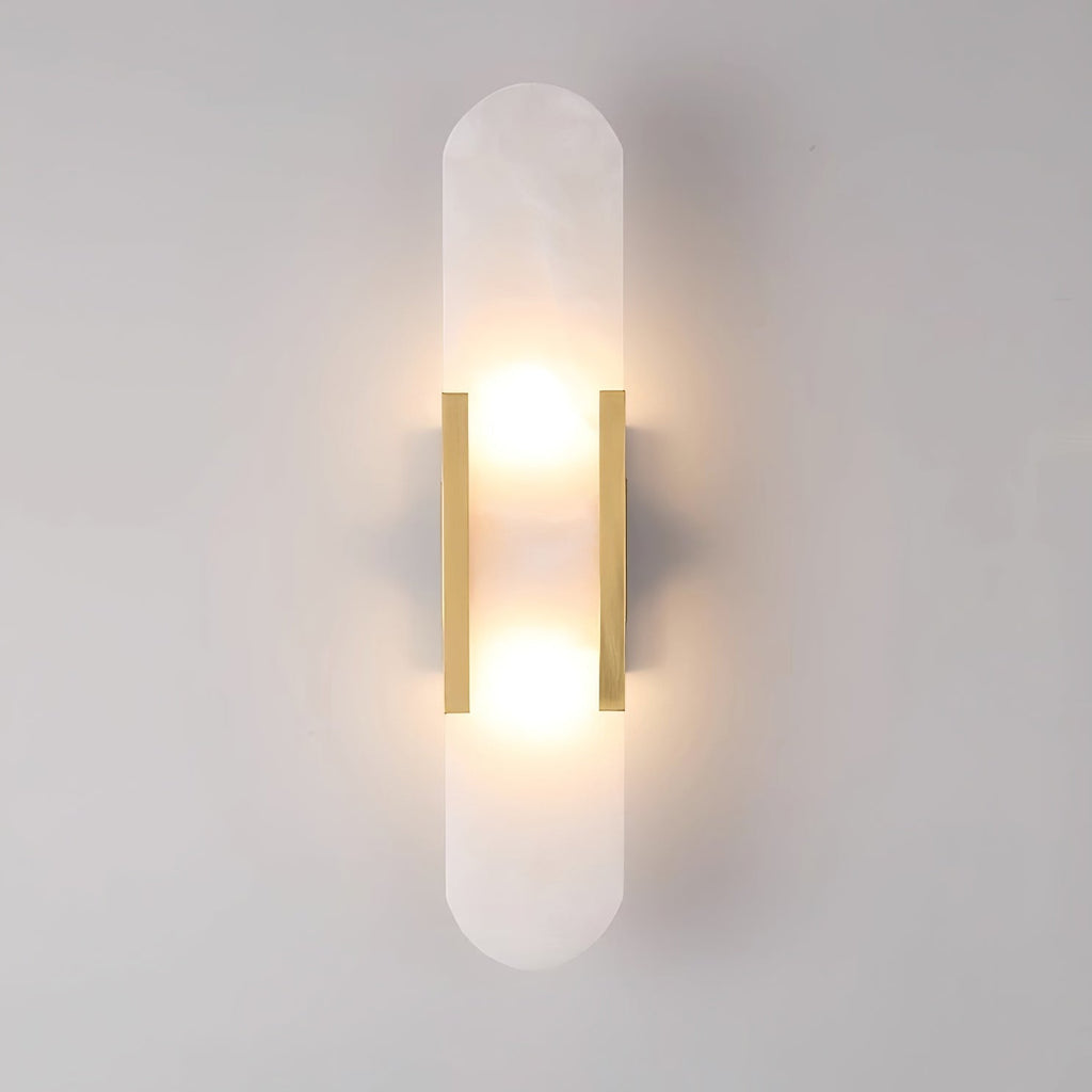 Clérachic Olraeia wall sconce in brass, both bulbs glowing behind the capsule alabaster panel on a pale grey wall