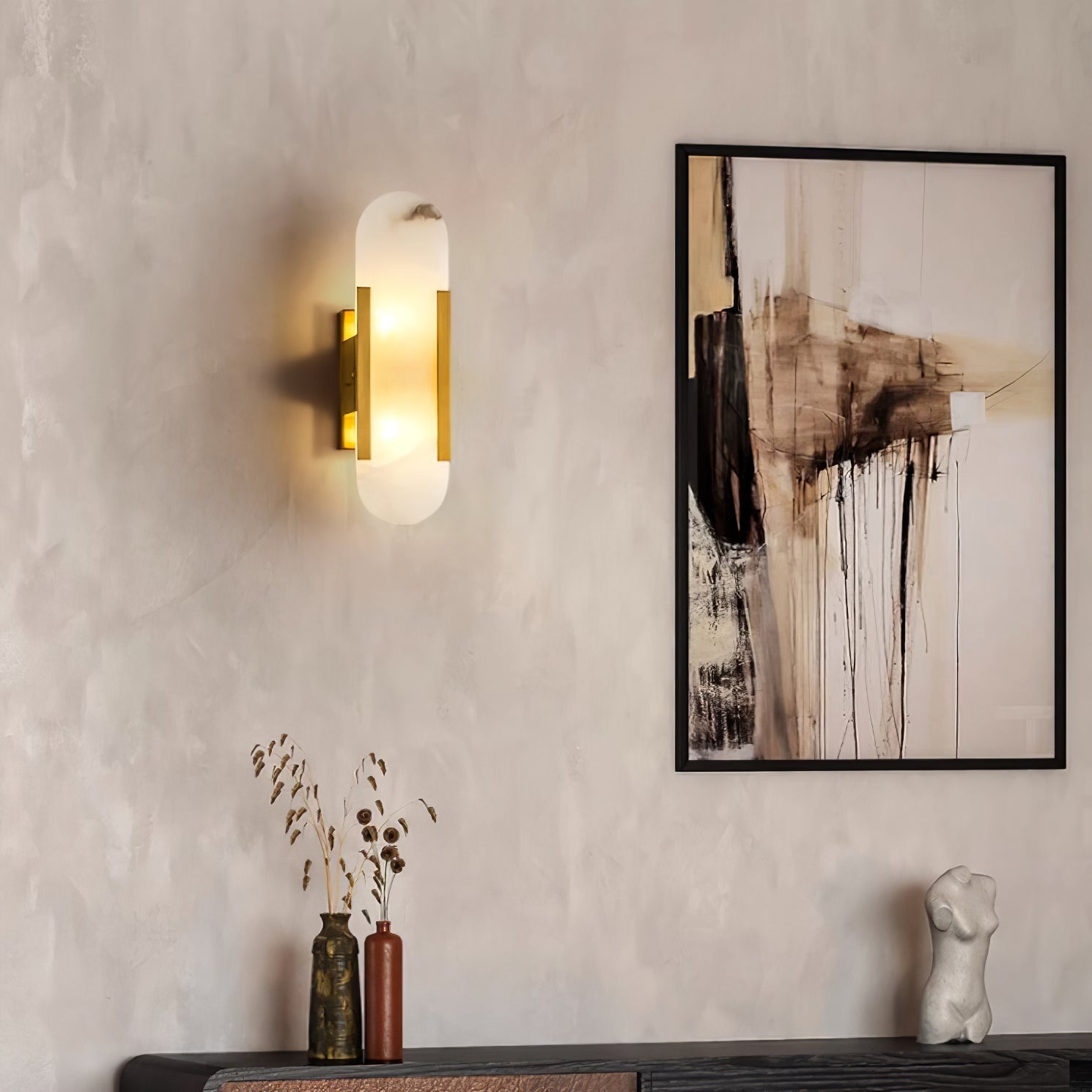 Clérachic sconce lit on a limewash plaster wall beside abstract art and a console of vases and dried stems