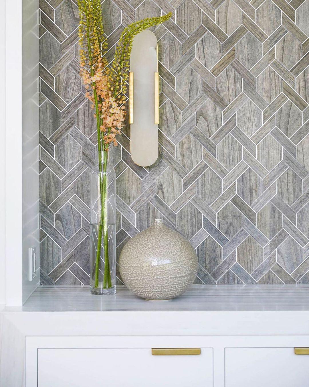 The Clérachic sconce mounted on a grey herringbone mosaic niche above a vase of flowers and white drawers