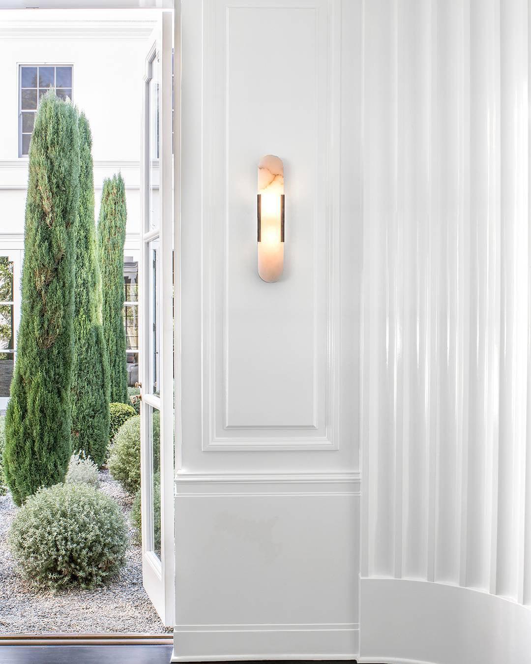 Clérachic sconce lit on a panelled hallway wall beside open doors onto a cypress-lined garden
