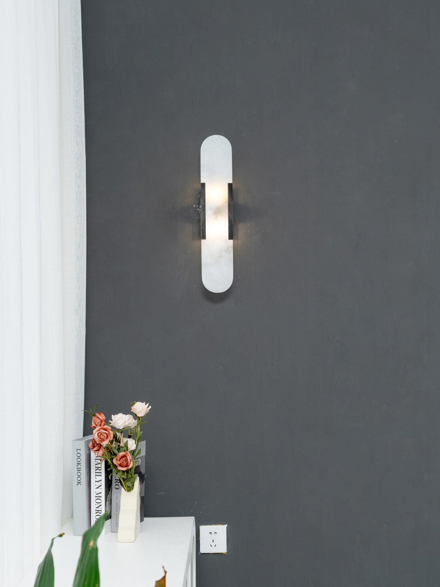 The Clérachic sconce with black bars on a charcoal wall, white sheer curtain and roses on the console beneath