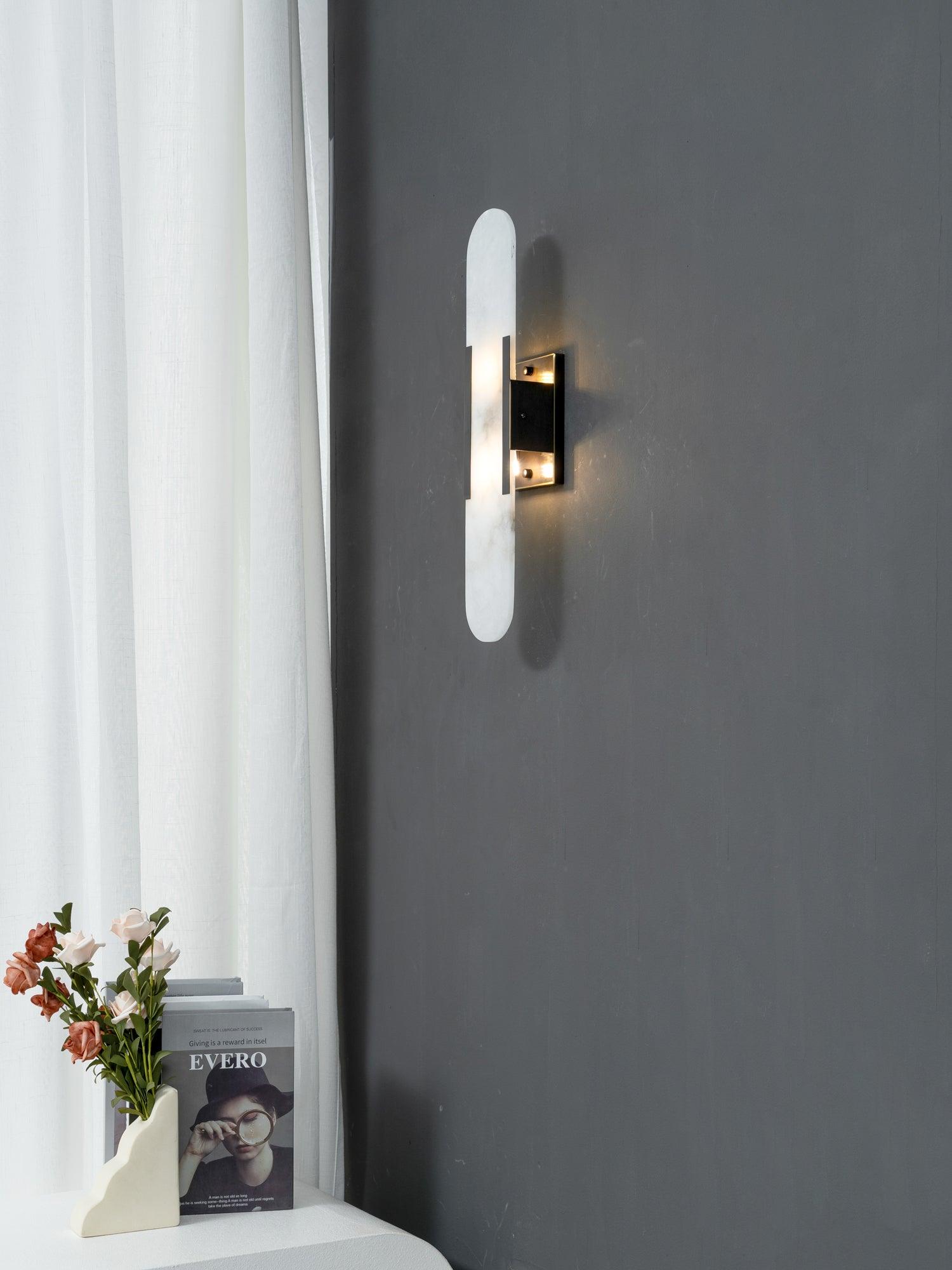 Clérachic sconce on a deep grey wall, its lit alabaster capsule set against a linen curtain and styled console